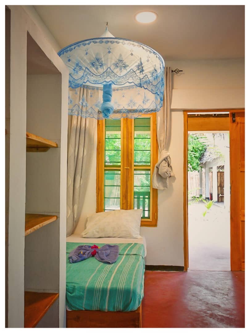 Single bed by the window with open door to the garden at Nanga