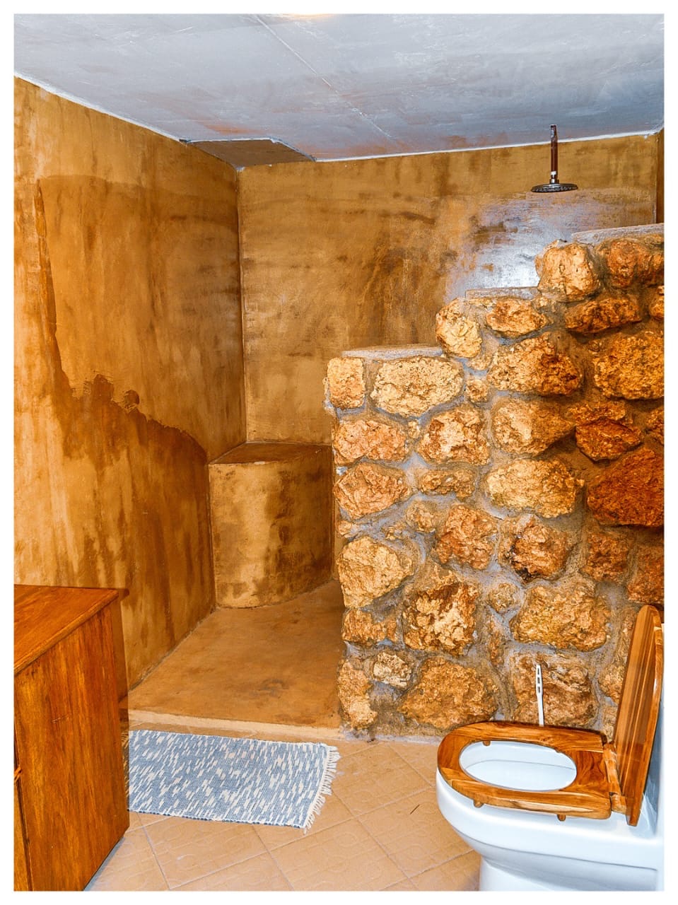 Open rain shower bathroom with coral stone wall in Mawimbi