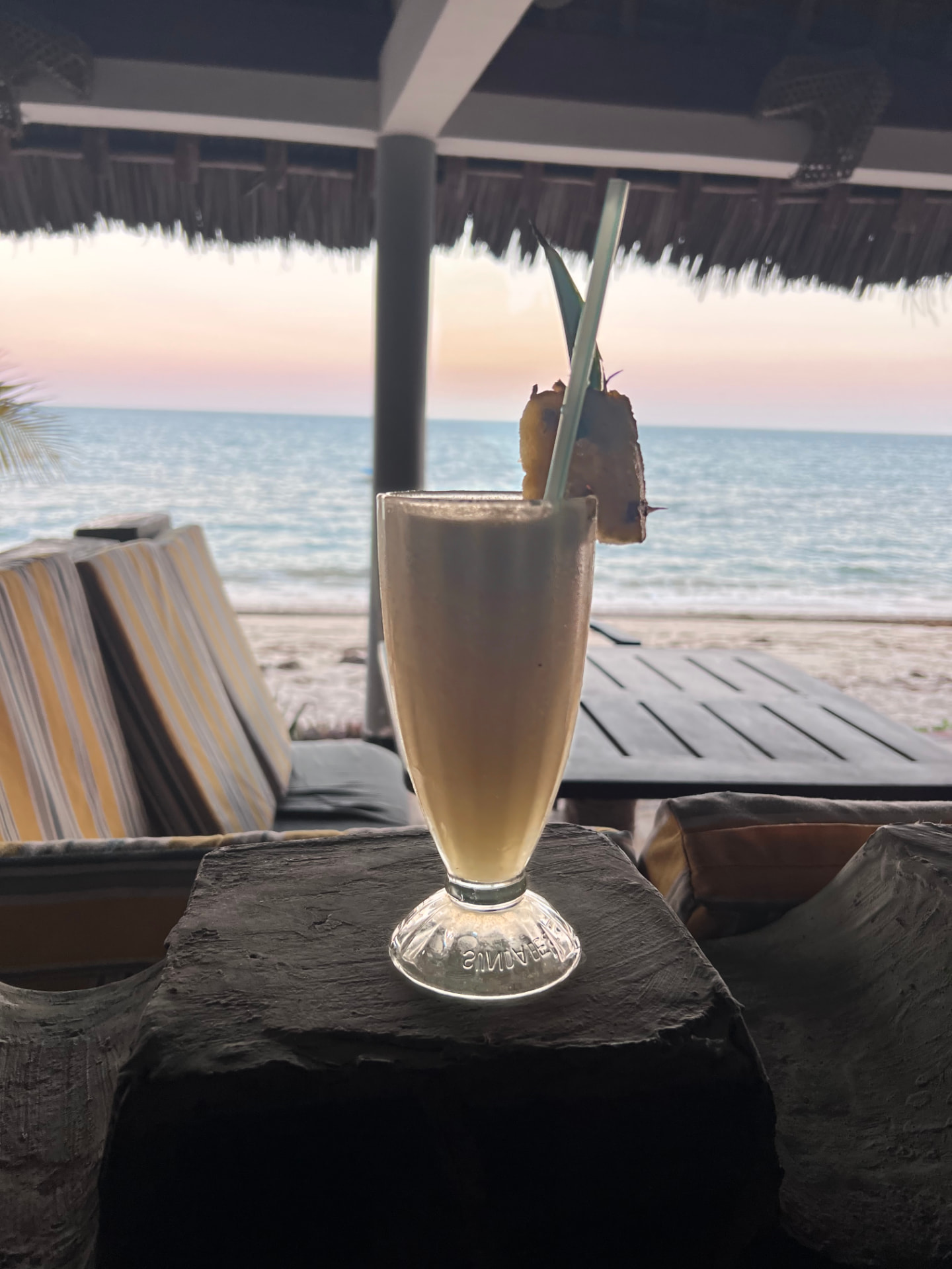 Piña Colada in a tall glass with the sea and pastel sunset behind