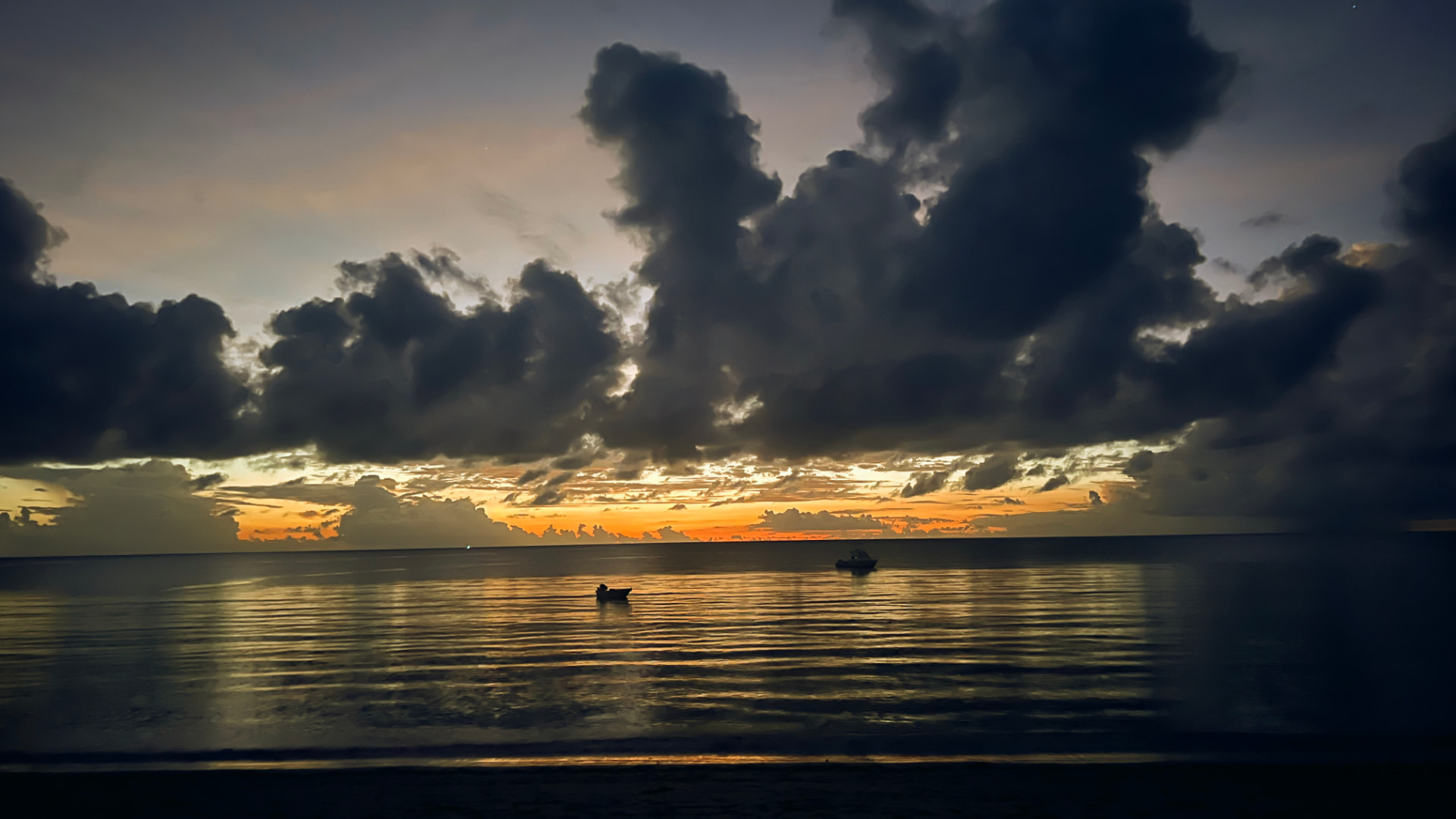Sunrise over the ocean with dark clouds and small boats at anchor