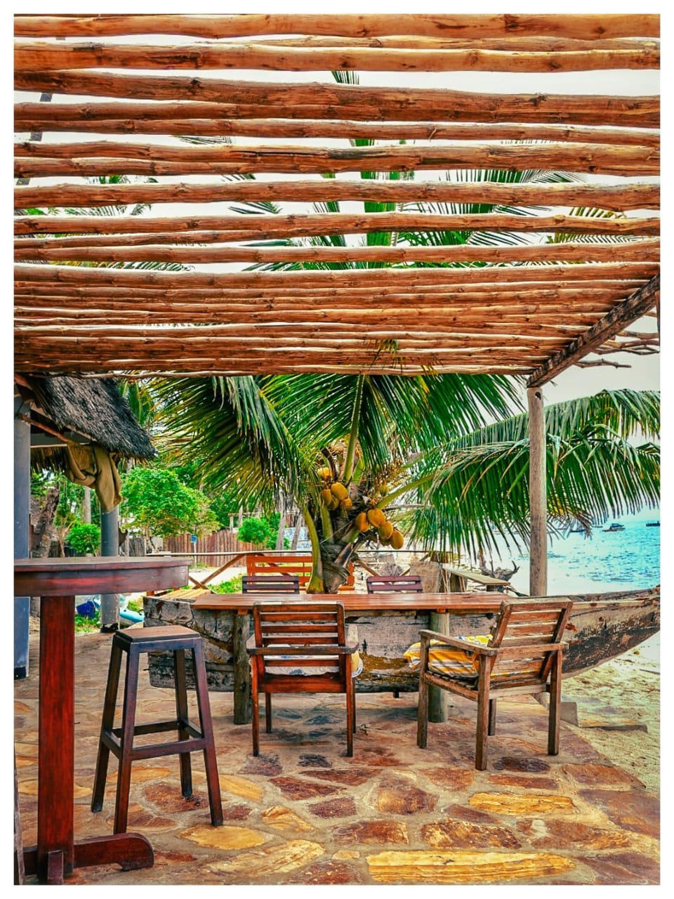 Wooden pergola with tables and chairs looking out over the palms to the sea