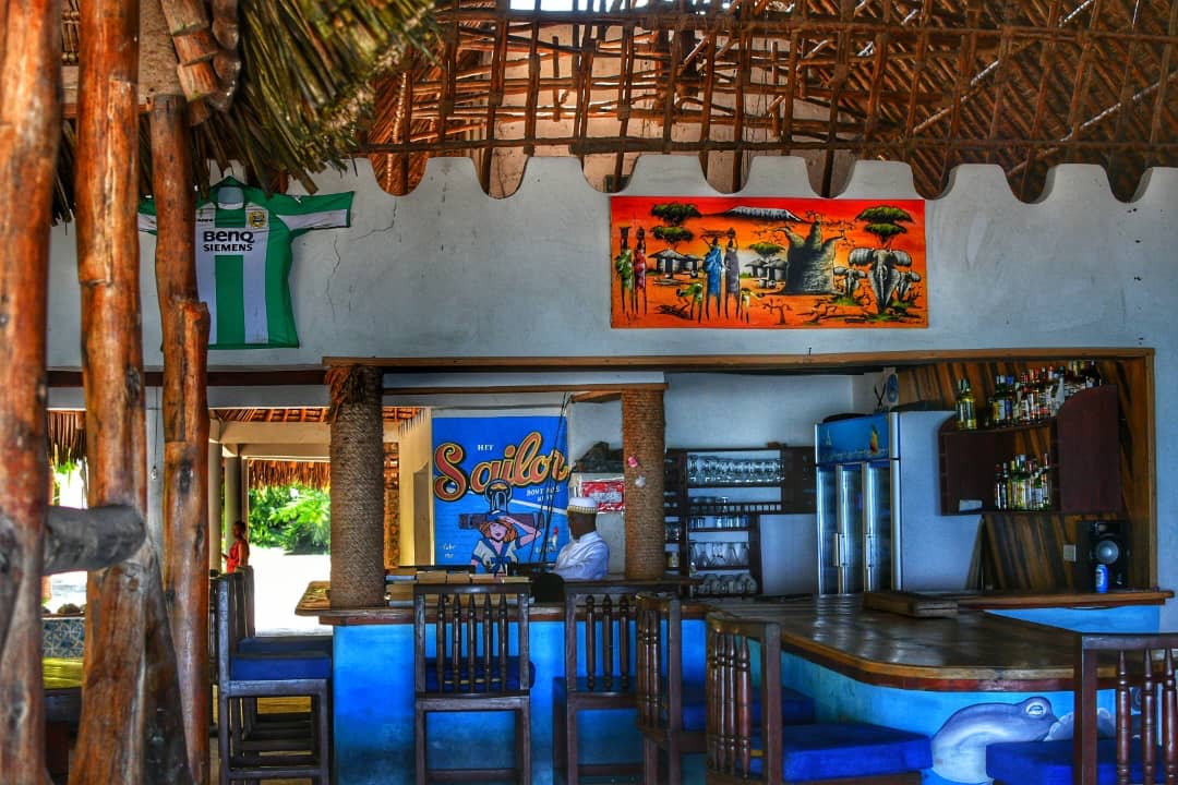 Open makuti bar with painted murals, bar stools and a stocked back bar