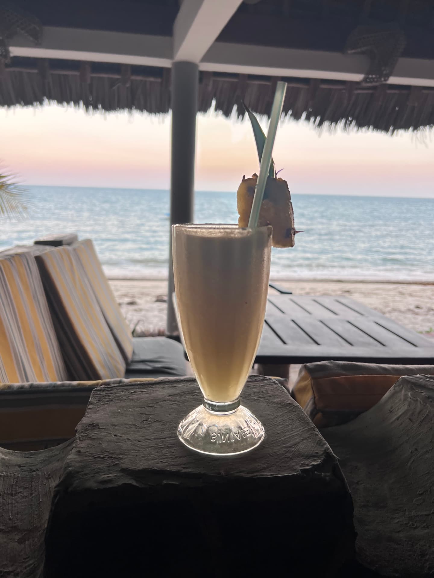 Fresh cocktail on a table under a makuti roof facing the sea